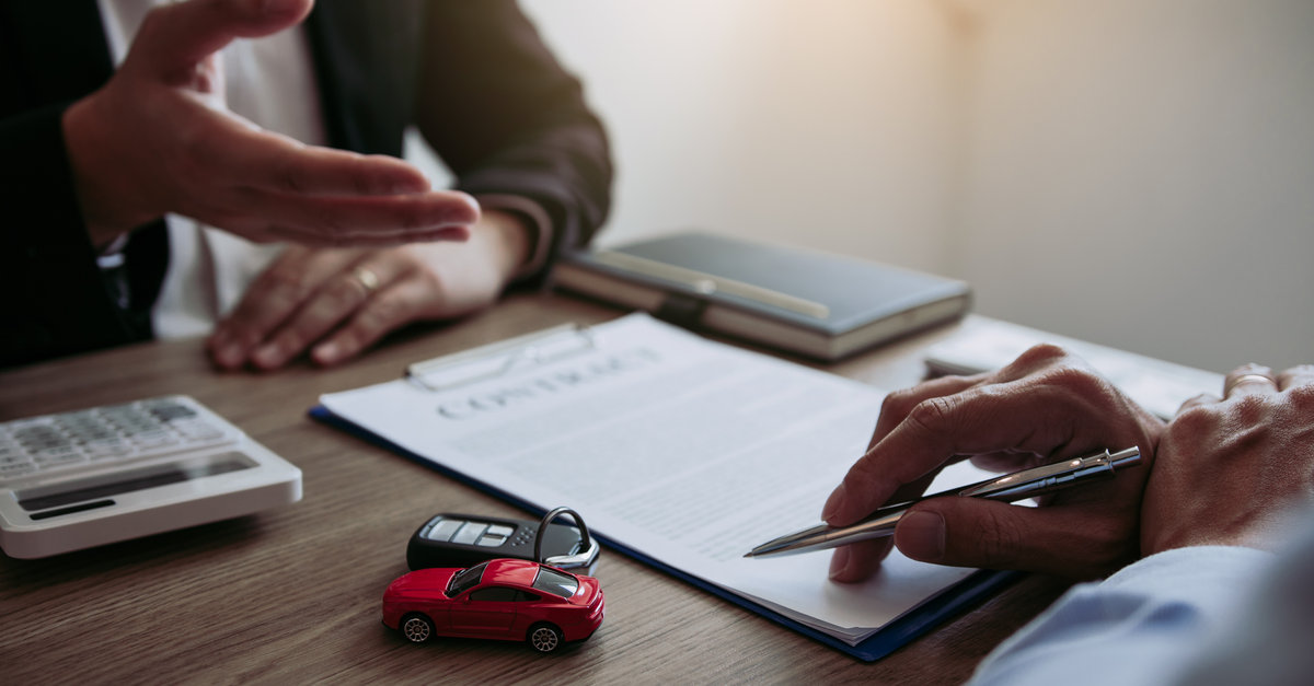 Finance Your New Vehicle | Man with pen, finance documents, calculator and car keys filling out paperwork to buy a new car